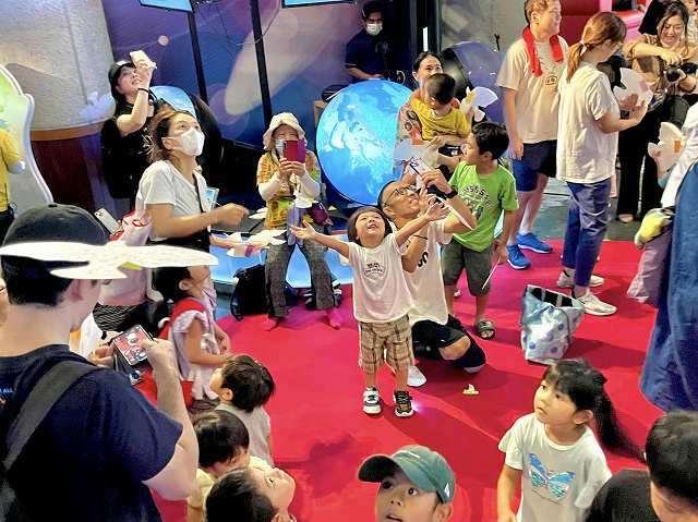 頭上から舞い降りるハト型の平和のメッセージをつかみ取る子どもたち